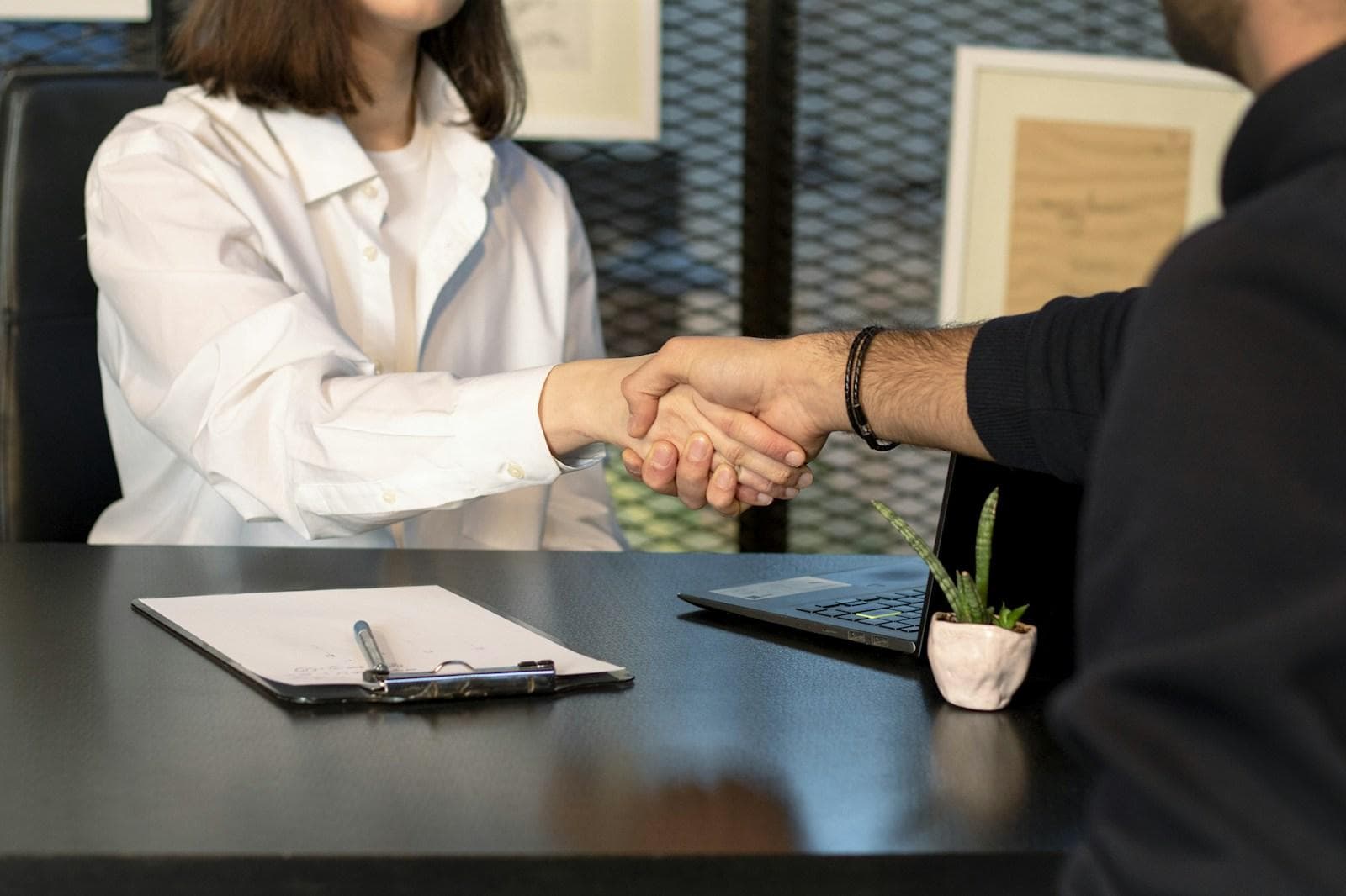 Two people shaking hands across a desk during a job interview