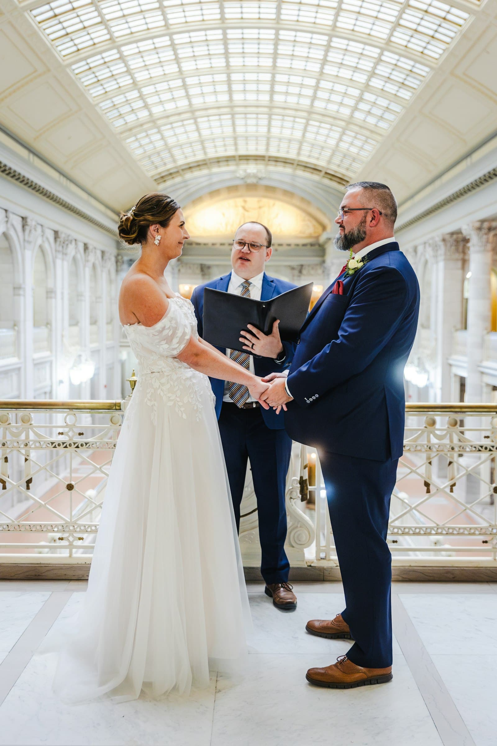 A bride and groom holding hands in front of an officiant