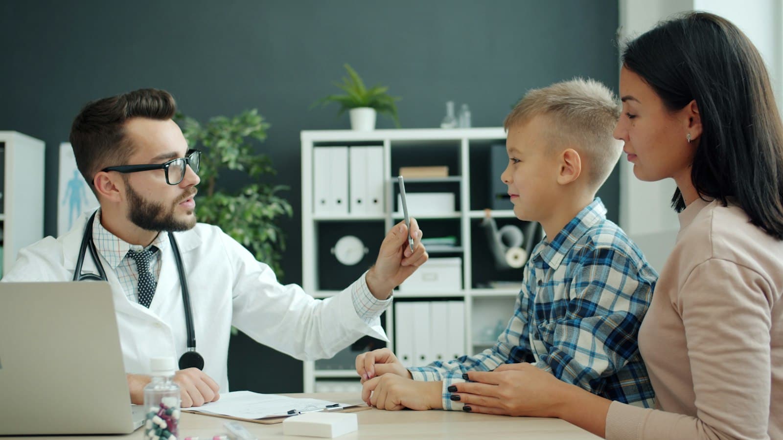 A doctor explaining something to a mother and her son in a clinic office